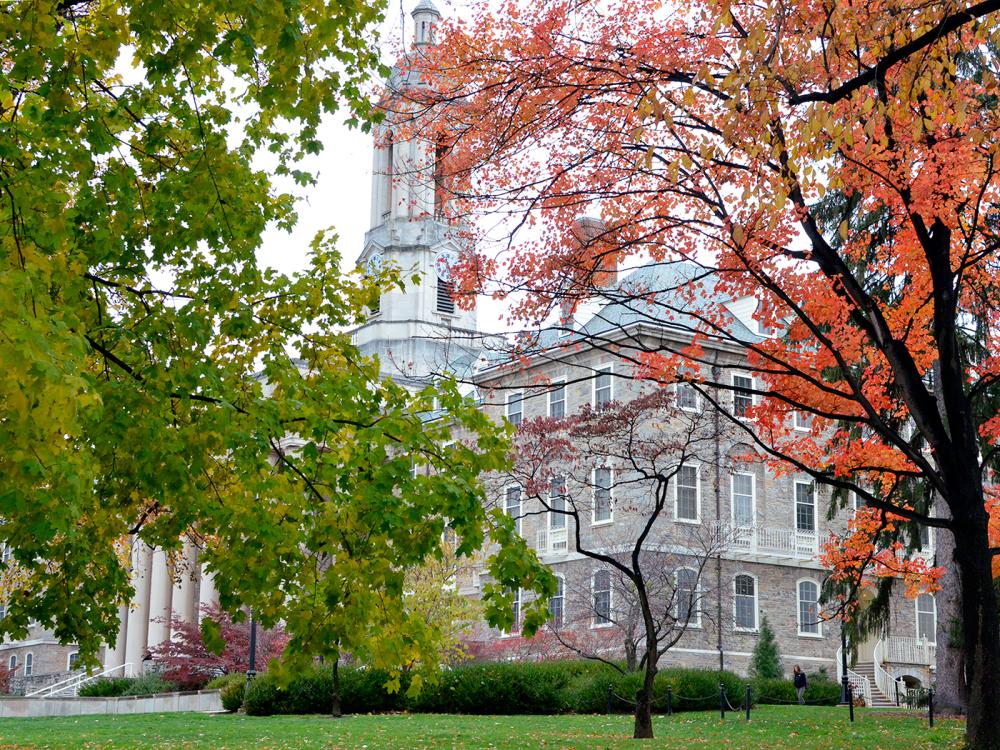 A picture of Old Main, an old stone building with trees on either side in orange and green colors.
